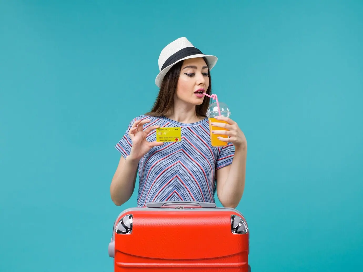 Vorderansicht einer Frau im Sommerurlaub auf Seereise, die einen Saft und eine gelbe Bankkarte hält, auf blauem Boden.